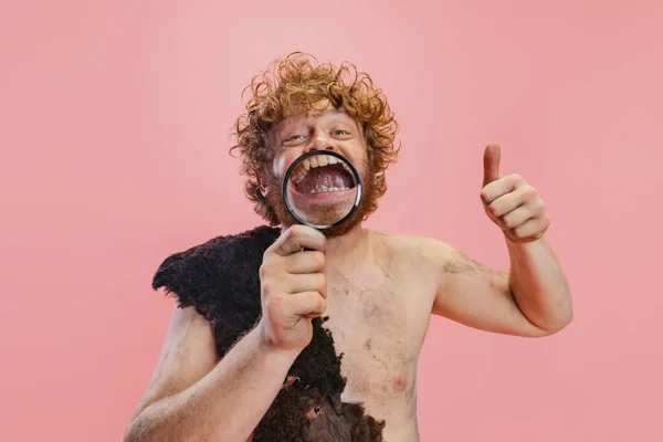 Portrait recadré de l'homme dans le caractère de la personne primitive, néandertalien tenant loupe dents agrandissantes isolé sur fond rose — Photo