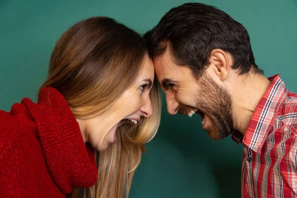 Gesneden zijaanzicht portret van paar staan, stoten hoofden tegen elkaar, schreeuwen en kijken naar elkaar geïsoleerd over groene achtergrond — Stockfoto