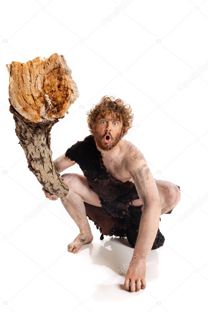 Full-length portrait of weird dirty man, neanderthal holding big wooden log isolated over white background