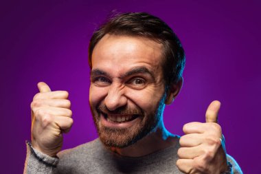 İnsanın yakın plan portresi heyecanla jest gibi görünüyor, mor arka planda, neon ışıklarıyla izole edilmiş poz veriyor.