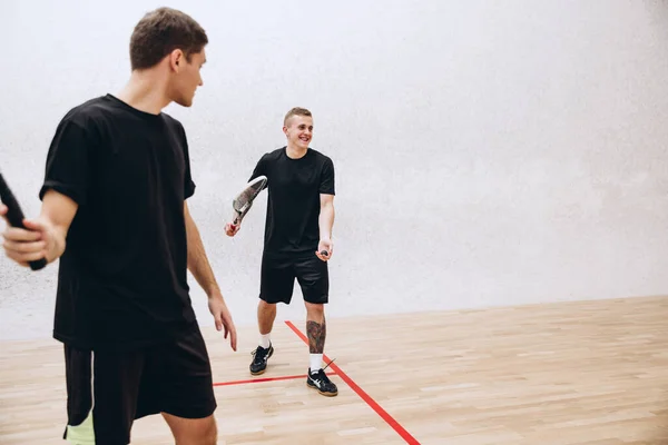 Ritratto ritagliato di due giovani uomini che giocano a squash isolati sullo sfondo dello studio sportivo — Foto Stock