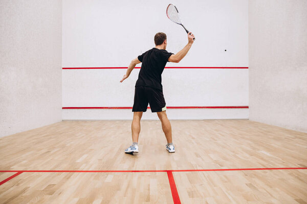 Back view of man playing squash game alone in sport studio