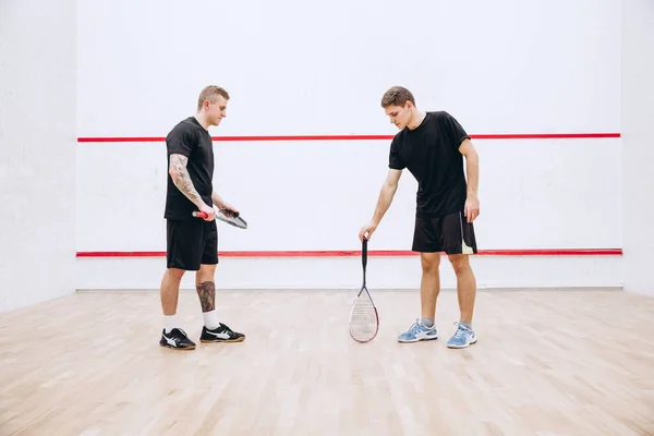 Full-legth portrait of two young sportive men at sport squash studio training, playing team game