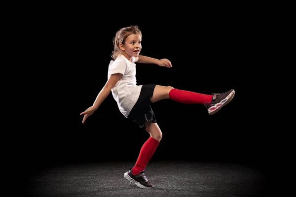 Retrato de larga duración de una niña deportiva en movimiento, entrenando, jugando al fútbol aislado sobre fondo negro —  Fotos de Stock