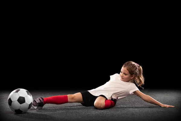 Teljes hosszúságú portré egy mozgásban lévő kislányról, edzés, focizás fekete háttérrel elszigetelve. Kapus. — Stock Fotó