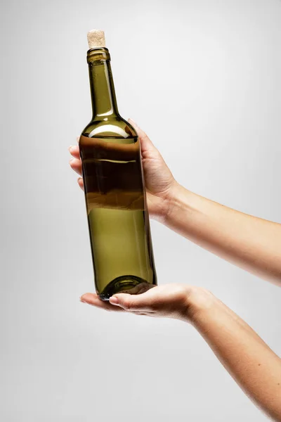 Imagem cortada de mão feminina segurando garrafa de vinho delicioso isolado sobre fundo cinza — Fotografia de Stock