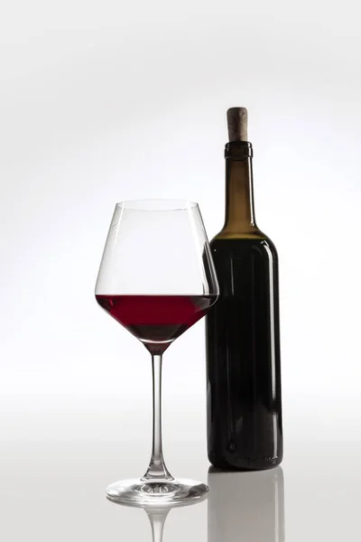 Image pleine longueur de bouteille de vin et verre rempli de vin rouge isolé sur fond gris — Photo