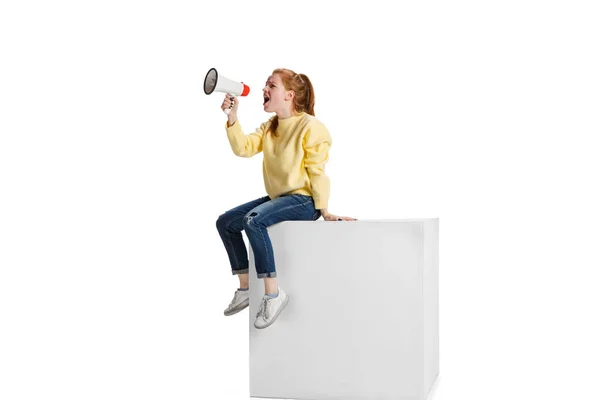Full-length portrait of young girl shouting in megaphone isolated over white background. Warning information — стоковое фото