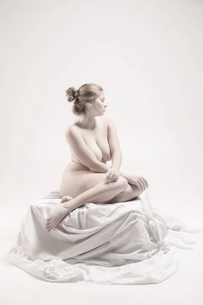 Ολο το μήκος πορτρέτο της νεαρής καλλιτεχνικής γυναίκας που ποζάρει γυμνή, κάθεται σε διαφανές πέπλο απομονωμένο πάνω από φώτα φόντο — Φωτογραφία Αρχείου