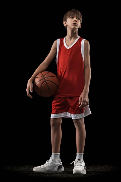Teljes hosszúságú portré tini fiú, kosárlabda játékos piros egyenruhában pózol labda elszigetelt fekete háttér — Stock Fotó