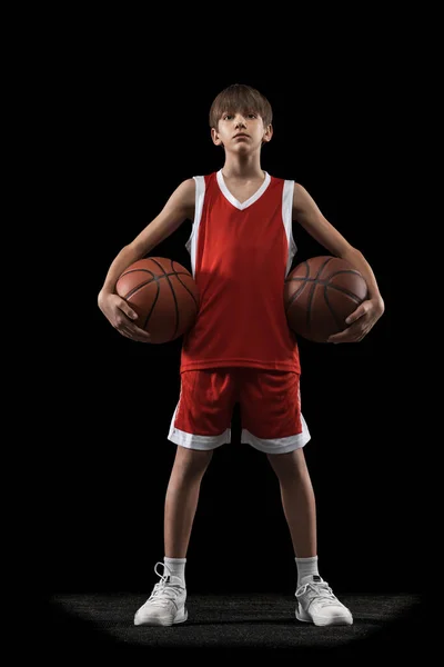 Ganztägiges Porträt von Teenager-Junge, Basketballspieler in roter Uniform posiert mit Bällen isoliert über schwarzem Hintergrund. — Stockfoto