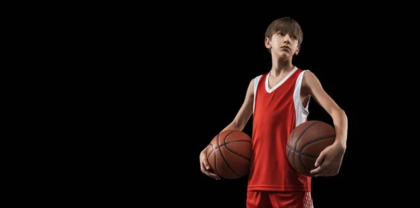 Ausgeschnittenes Porträt eines kleinen Jungen, Basketballspieler in roter Uniform stehend, mit Ball isoliert über schwarzem Hintergrund posierend. Fley — Stockfoto