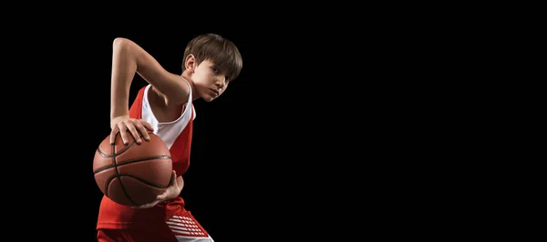 Estúdio recortado tiro de menino, jogador de basquete em uniforme posando com bola em ação isolado sobre fundo preto. Folheto — Fotografia de Stock