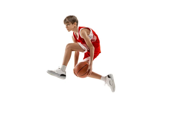 Full-length side view studio shot van jonge jongen, basketbalspeler in rood uniform training geïsoleerd over witte achtergrond. In een sprong — Stockfoto