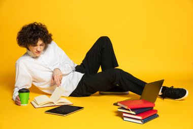 Genç bir çocuğun portresi, yerde yatan bir öğrenci, kitap okuyor, sarı arka planda izole edilmiş ödevler yapıyor.