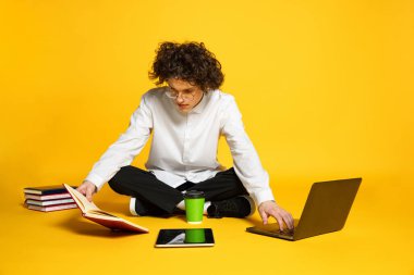 Genç bir adamın portresi, konsantre öğrenci, sınavlara hazırlanıyor, sarı stüdyo arka planında izole bir şekilde kitap okuyor.