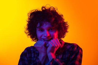 Genç kıvırcık adamın portresi, heyecanlı duyguları olan, neon renkli sarı turuncu arka planda izole edilmiş öğrenci.