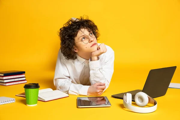 Portrét mladého kadeřníka v brýlích, přemýšlivého studenta ležícího na podlaze a provádějícího domácí úkoly izolované přes žluté pozadí studia — Stock fotografie