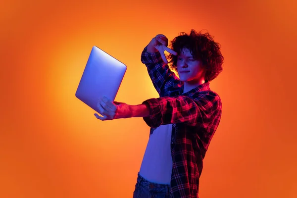 若いですカールマンの肖像画で小切手シャツ持っていますオンラインコール上の友人とノートパソコン上で隔離された上でオレンジの背景で青ネオンライト — ストック写真