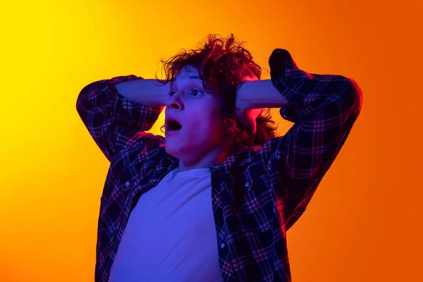 Porträt eines jungen, lockigen Mannes im karierten Hemd, der Schockgefühle isoliert vor orangefarbenem Hintergrund im Neonlicht zeigt — Stockfoto