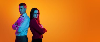 Sırt sırta duran iki genç insan portresi. Turuncu stüdyo arka planında neon ışıkta izole edilmiş. El ilanı