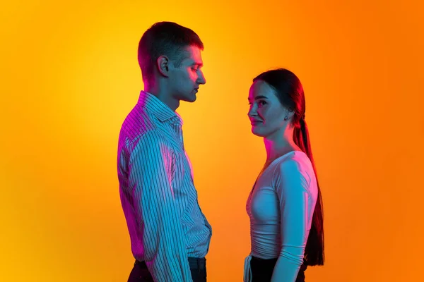 Retrato de dois jovens, homem e mulher em pano branco calmamente em pé, posando isolado sobre fundo laranja em néon azul — Fotografia de Stock