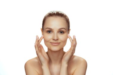 Mükemmel pürüzsüz ciltli genç bir kadının portresi kameraya bakıyor, beyaz stüdyo arka planında izole edilmiş poz veriyor.