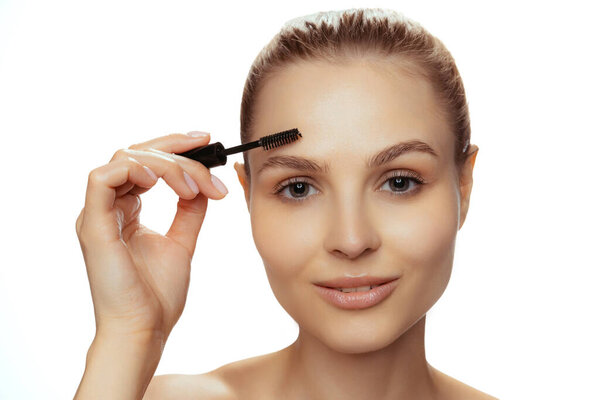 Portrait of young beautiful woman with natural makeup using brow mascara isolated over white studio background