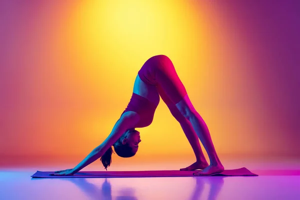 Portrait de jeune fille sportive faisant des exercices d'étirement isolé sur fond rose et jaune dégradé au néon — Photo