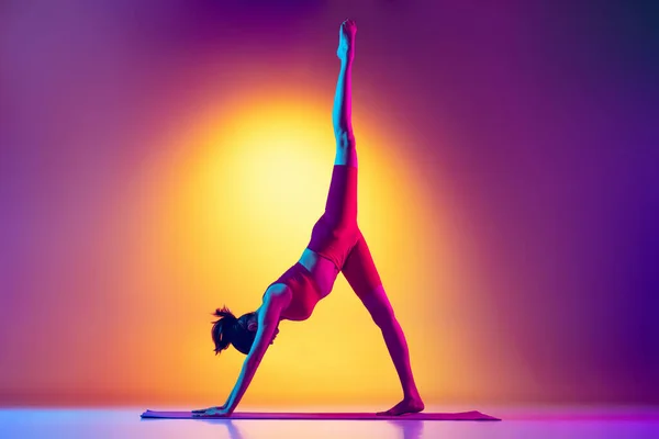 Portrait de jeune fille sportive faisant des exercices de yoga, la jambe montant isolé vers le haut sur dégradé fond rose et jaune au néon. — Photo