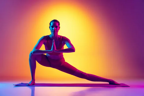 Portrait de la formation des jeunes filles, faire des exercices d'étirement et de yoga isolé sur dégradé fond rose et jaune au néon — Photo