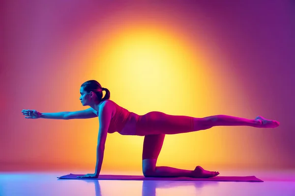 Portrait de jeune fille mince formation, faire des exercices d'étirement et de yoga isolé sur dégradé fond rose et jaune au néon — Photo