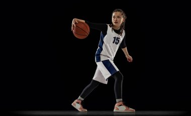 Genç bir kızın portresi, hareket halindeki basketbolcu, siyah stüdyo arka planında izole edilmiş top sürüyor.