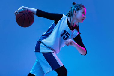Basketbol oynayan genç bir kızın portresi, neon ışıkta mavi arka planda izole edilmiş eğitim.