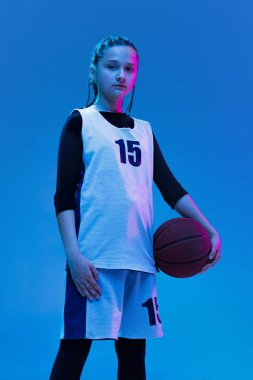 Genç bir kızın portresi, üniformalı bir basketbolcu mavi stüdyo arka planında izole bir şekilde poz veriyor.