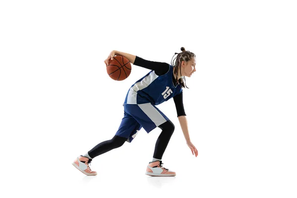 Full-length side view studio shot of young girl, basketball player in blue uniform training isolated over white background. Dribbling — Stockfoto