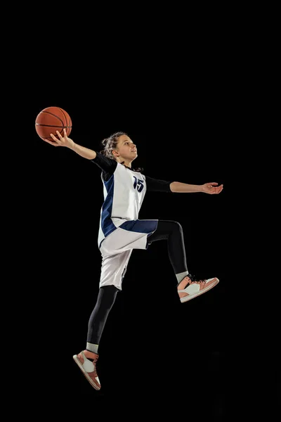 Jump shot. Scoring a goal. Portrait of teen girl, basketball player in motion, training, playing isolated over black background. — Stockfoto