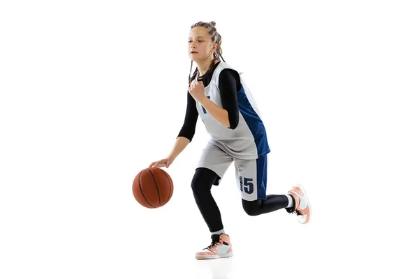 Studio shot of young girl, basketball player in blue uniform training isolated over white background. Dribbling ball before throwing — Stockfoto