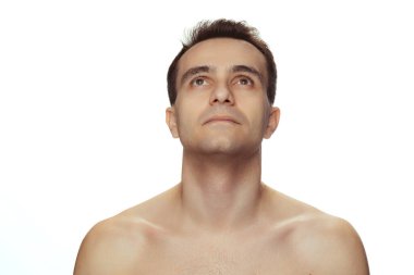 Temiz yüzlü genç yakışıklı bir adam portresi, mükemmel bir ten, üstsüz poz, beyaz stüdyo arka planında izole bir şekilde yukarı bakıyor.