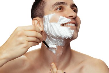 Beyaz stüdyo arka planında sakallı, tıraş olmuş, yüzü krem ve jiletle tıraş olmuş genç bir adamın portresi. Yumuşak ten