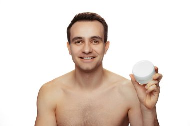 Beyaz arka planda izole edilmiş deri tahrişinden kaçınmak için tıraş olduktan sonra yüz kremi süren genç bir adamın portresi.