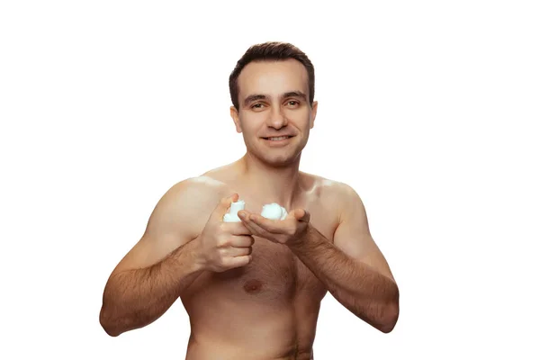 Portrait of young shirtless man applying shaving cream on hand isolated over white studio background — ストック写真