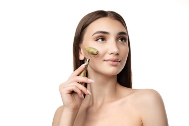 Portrait of beautiful young girl using face cosmetology tool, roller for massage isolated over white background