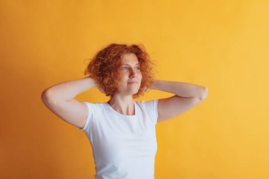 Parlak mavi gözlü, kıvırcık saçlı güzel kızıl saçlı kadının portresi sarı stüdyo arka planında izole edilmiş poz veriyor.