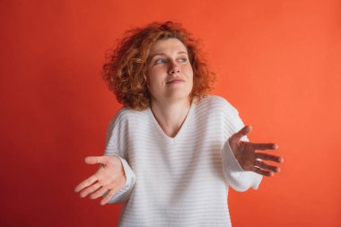 Kızıl saçlı genç bir kadının portresi kırmızı stüdyo arka planında izole edilmiş yüz ifadesi sergiliyor.