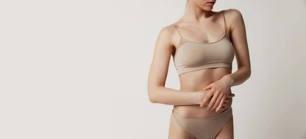 Primo piano sottile corpo femminile sportivo, pancia in biancheria intima beige isolato su sfondo grigio. — Foto Stock