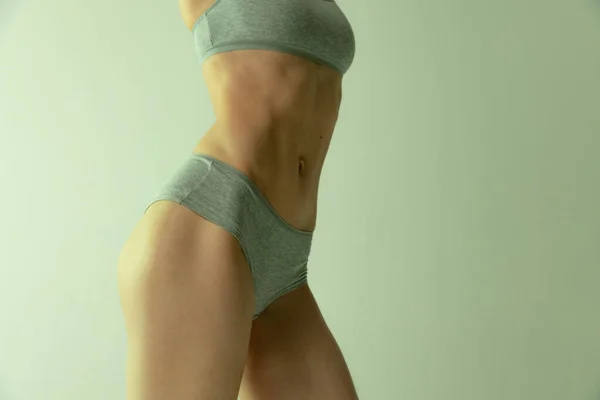 Cropped image of slim muscular female body in cotton underwear isolated over grey studio background. Fit body — 스톡 사진