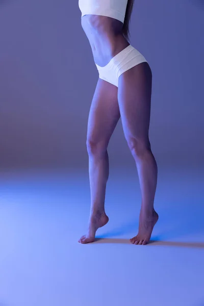 Спортивні гладкі жіночі ноги в білій білизні позують ізольовані на синьому студійному фоні в неоновому світлі . — стокове фото