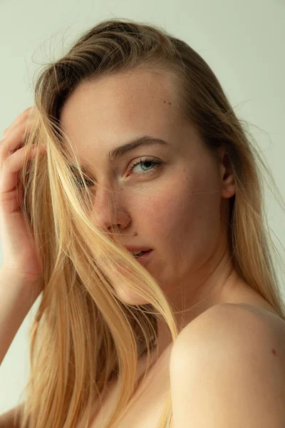 Portrait of beautiful young woman with light green eyes tenderly looking at camera, posing isolated over grey studio background — Foto de Stock