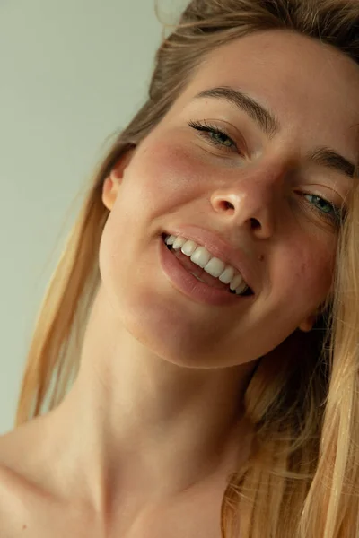 Portrait of young beautiful woman with blush cheeks barely smiling, posing isolated over grey studio background — Foto de Stock